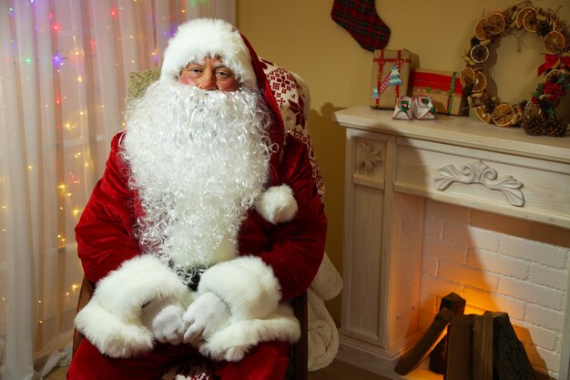 Papai noel sentado em uma cadeira confortável perto da lareira em casa