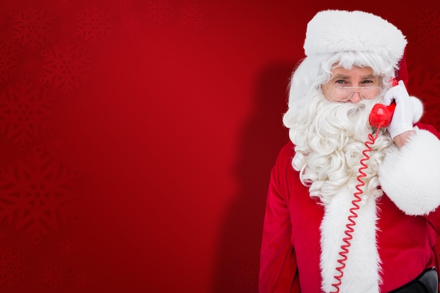 Papai noel sorridente ao telefone contra o fundo vermelho do floco de neve