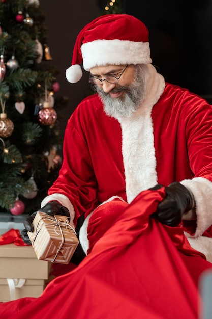 Papai Noel sorridente com luvas de couro e fantasia vermelha roubando presentes enquanto destrói o Natal