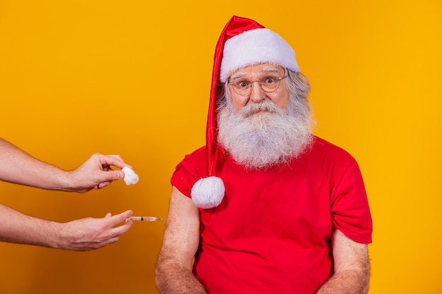 Papai noel usando máscara facial sendo vacinado com injeção