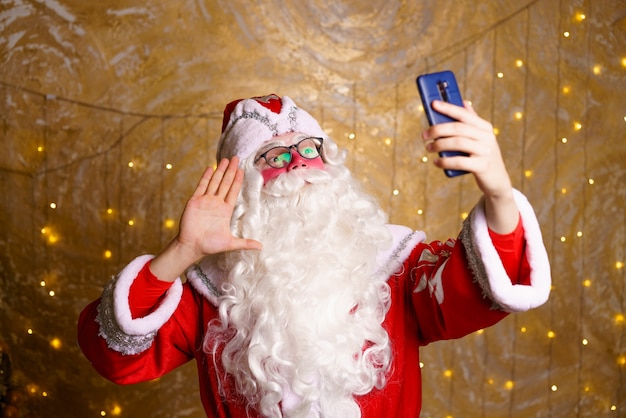 Papai noel usando telefone celular na época do natal tira uma selfie ou se comunica por vídeo comunic ...