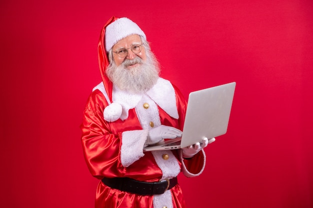 Papai Noel usando um laptop sobre fundo vermelho.