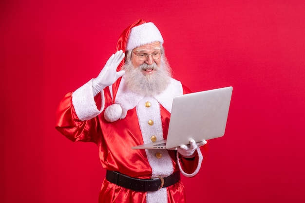 Papai Noel usando um laptop sobre fundo vermelho.