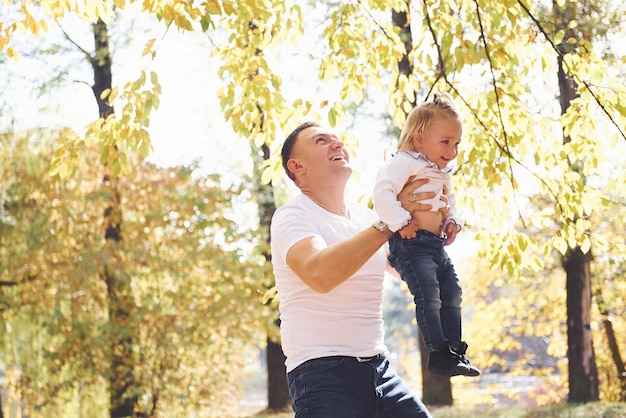Papai segura a filha nas mãos e divirta-se no parque outono.