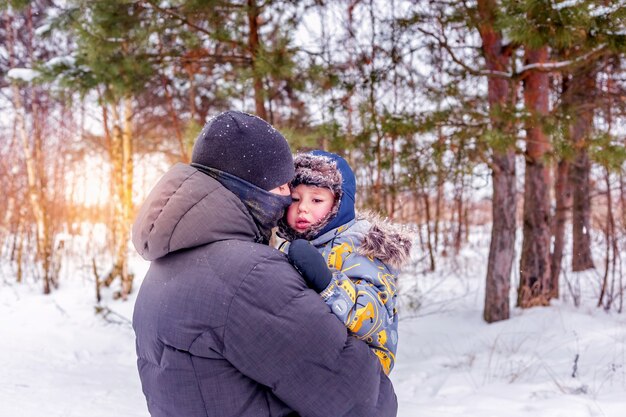 Papai segura e abraça o filho pequeno em um bosque nevado ou parque de inverno. conceito de atividades ao ar livre de inverno para a família.