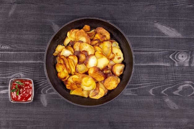 Papas fritas caseras fritas en una sartén de hierro fundido antiguo vintage y salsa de tomate sobre un fondo rústico de madera. Vista superior.