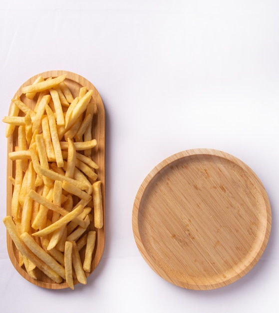 Papas fritas colocadas en una placa de madera larga y una placa de madera redonda vacía, vista superior.