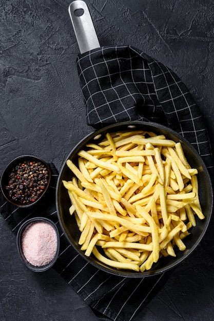 Papas fritas congeladas en una sartén. Fondo negro. Vista superior. Espacio para texto