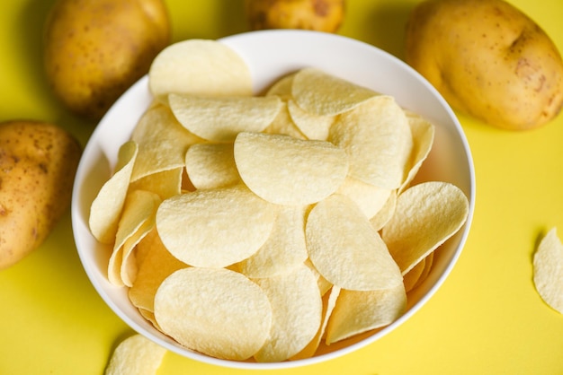 Papas fritas crujientes en la mesa de la cocina y papas crudas frescas sobre fondo amarillo Merienda de papas fritas en un tazón