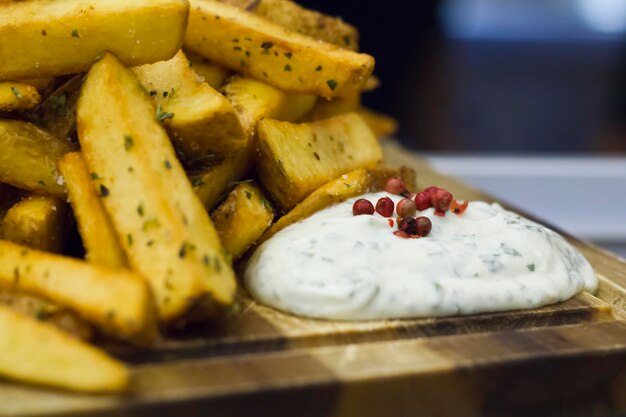 papas fritas fritas con orégano y salsa blanca de ajo servidas en una tabla de madera