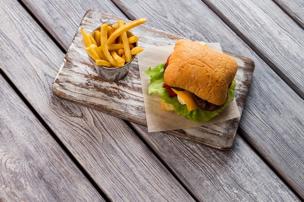 Papas fritas y hamburguesa a bordo. Bollos y hojas de lechuga. Ejemplo de platos de comida rápida. Receta secreta de hamburguesa con queso.