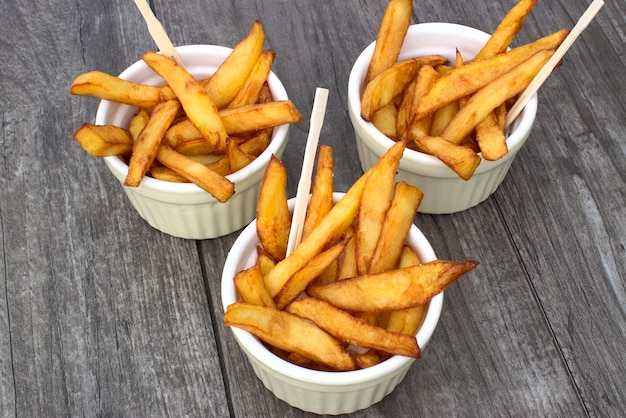 Papas fritas hechas en casa en los cuencos para los bocados en fondo de madera.