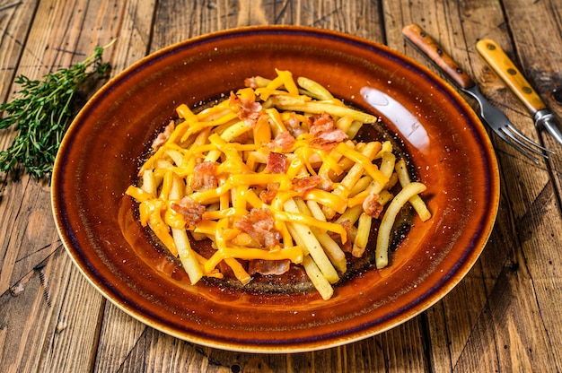 Papas fritas con queso cheddar derretido y tocino servido en un plato rústico