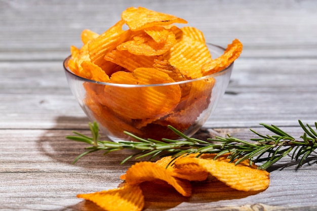 Papas fritas con una ramita de romero en un recipiente de vidrio sobre una mesa de madera