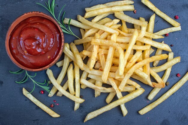 Papas fritas con salsa de tomate en placa de piedra negra, vista superior.