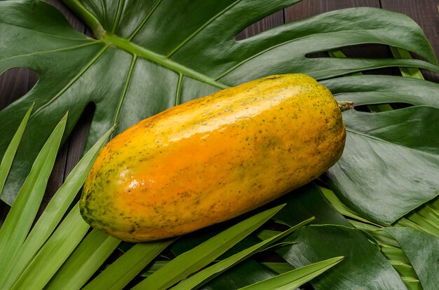 Papaya en hojas de palma en un fondo de madera oscuro.