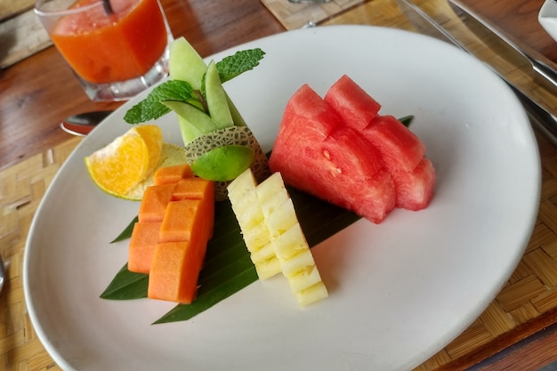 Papaya, piña, melón, sandía, naranja con limón y menta en un plato blanco Almuerzo de frutas de verano
