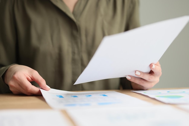 Papéis de check-ups de gerente feminino com estatísticas de dados de negócios sentados no local de trabalho na empresa