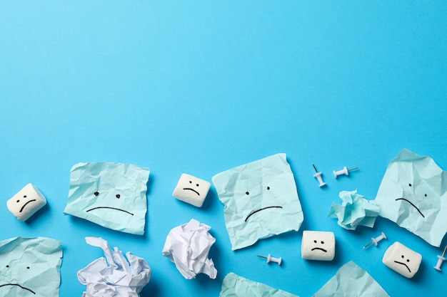 Papéis e marshmallows com emoji triste em espaço de fundo azul para texto