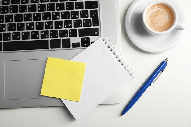 Papel adesivo amarelo vazio em caneta de teclado de laptop e copo de café em fundo de mesa
