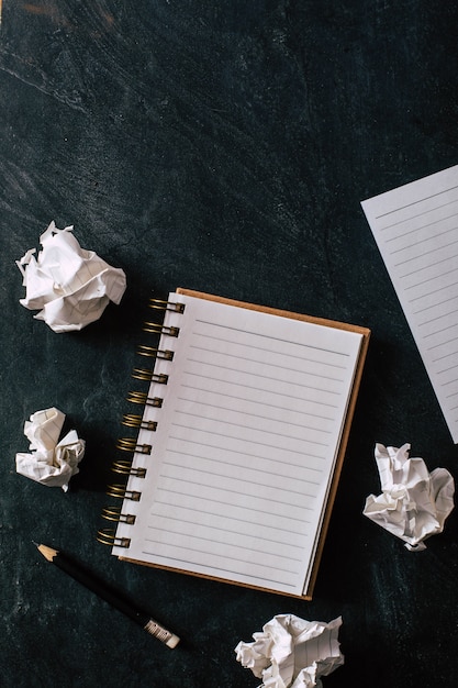 papel amassado com caderno e lápis sobre fundo preto