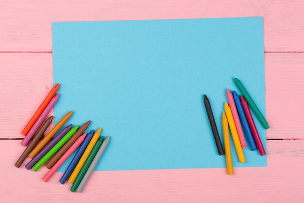 Papel azul en blanco y lápices de colores sobre una mesa de madera rosa