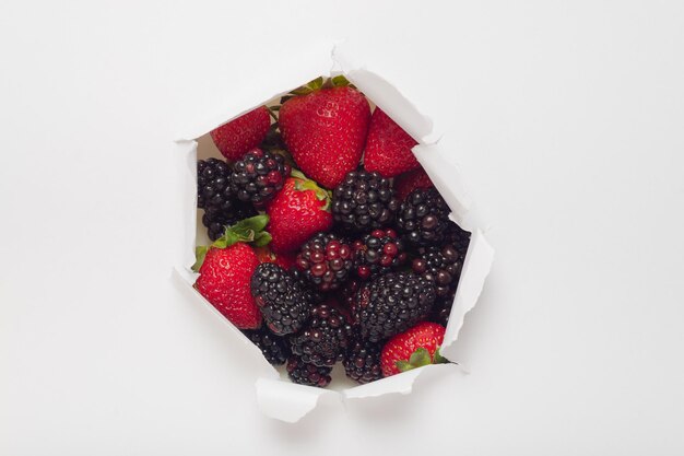 Foto papel blanco con agujero rasgado que revela moras y fresas frutas de temporada