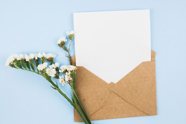 Foto papel en blanco blanco en el sobre marrón con flores blancas sobre fondo azul