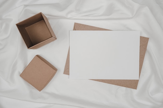 Papel blanco en blanco sobre papel marrón y caja de cartón puesta sobre tela blanca