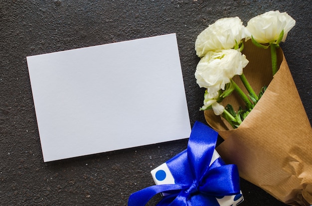 Papel en blanco, caja de regalo y ramo de flores blancas