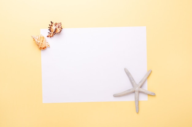 Foto papel en blanco, conchas y estrellas de mar sobre fondo amarillo. concepto de planificación de vacaciones y vacaciones de verano