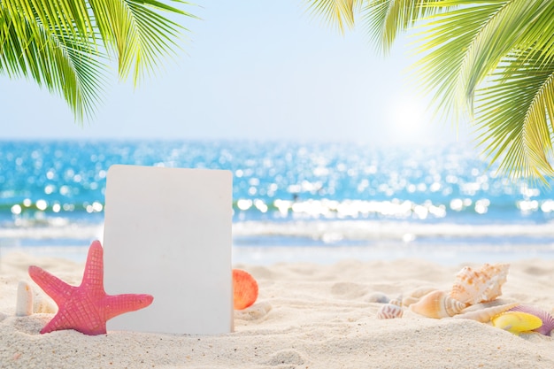 Foto papel en blanco con conchas en la playa de arena