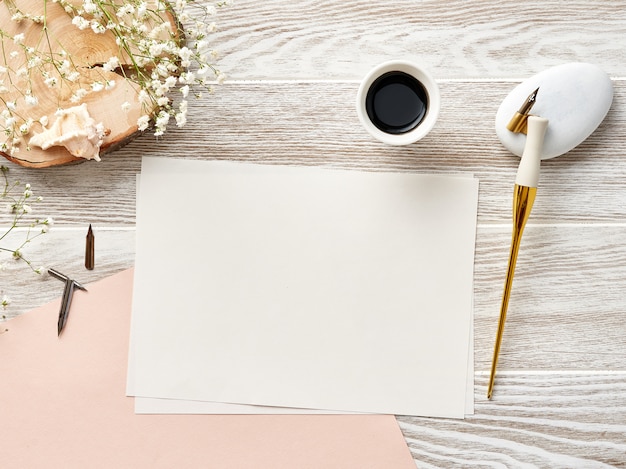 papel en blanco para invitación o carta sobre fondo blanco de madera con pluma y tinta de caligrafía. Vista desde arriba.