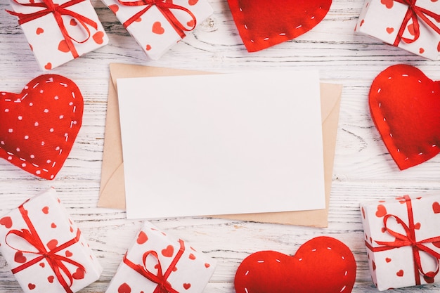 Foto papel en blanco rodeado de cajas de regalo envueltas con cintas y corazones textiles