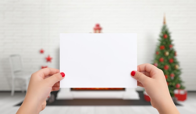 Papel en blanco para la tarjeta de felicitación de Navidad Año Nuevo en manos femeninas En el fondo hay un árbol de Navidad con adornos