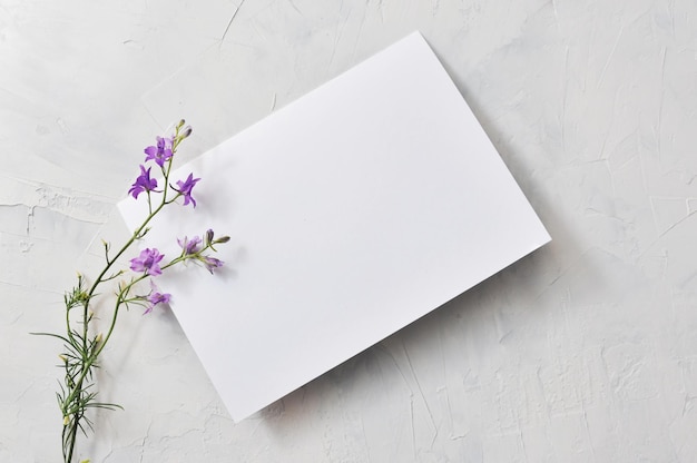 Papel blanco vacío con un lugar para escribir sobre un fondo gris y flores al lado