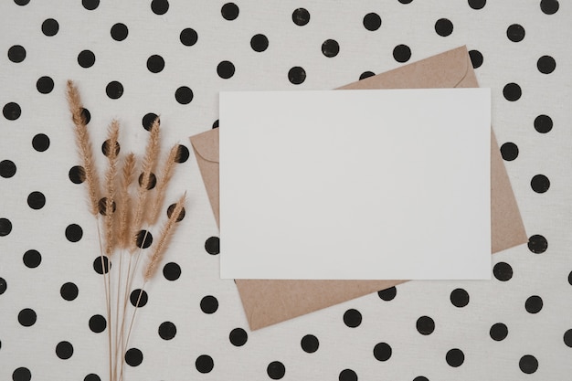 Papel branco em branco em envelope de papel pardo com flor seca de rabo de raposa eriçada e caixa de papelão em pano branco com pontos pretos