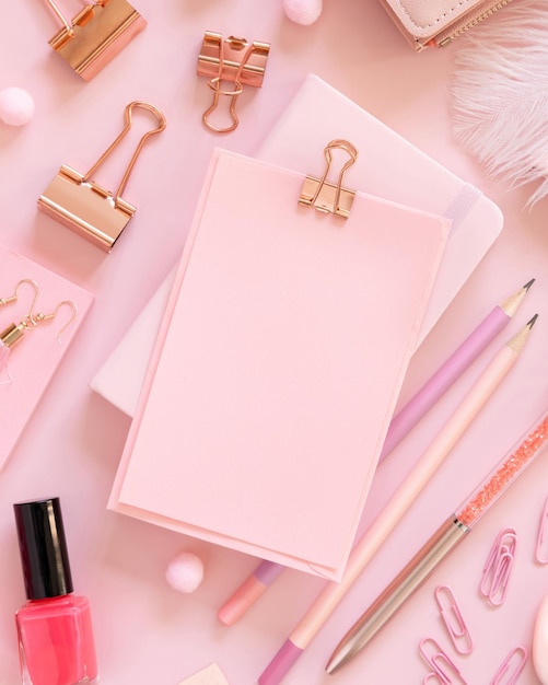 Foto papel con un clip y accesorios escolares rosa en maqueta de vista superior rosa pastel lugar de trabajo femenino con tijeras, lápices, bolígrafos, clips, pendientes y esmalte de uñas concepto de regreso a la escuela