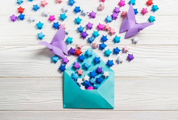 Papel colorido origami sorte papel estrelas e borboletas em envelope azul na madeira branca