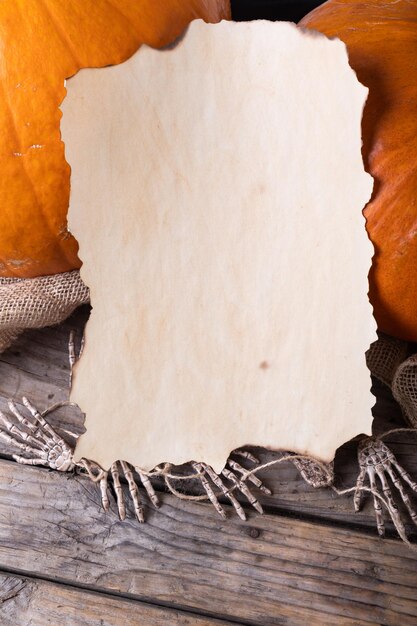 Foto papel com espaço de cópia contra abóboras e mãos de esqueleto em superfície de madeira contra fundo cinza. conceito de festividade e celebração de halloween