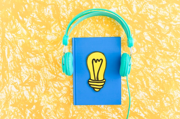 Foto papel cortado lâmpada amarela no notebook fechado com fone de ouvido no plano de fundo texturizado
