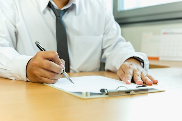 Papel de assinatura do contrato do homem de negócios com a pena na mesa de escritório.