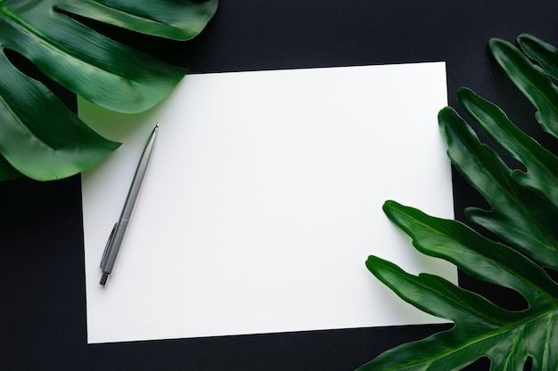 Foto papel de carta branco em branco com folhas tropicais sobre a mesa preta fundo de design do espaço de trabalho em casa vista plana do laytop