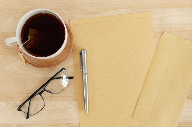 Papel de carta em branco e xícara de chá de envelope na mesa de escritório de madeira