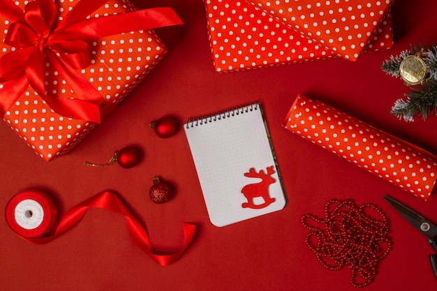 Papel de embrulho vermelho, fitas, bloco de notas, tesouras e caixas de presente em cima da mesa. O conceito das próximas férias de Natal.