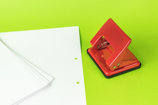 Papel de escrita branco e um furador vermelho sobre um fundo verde