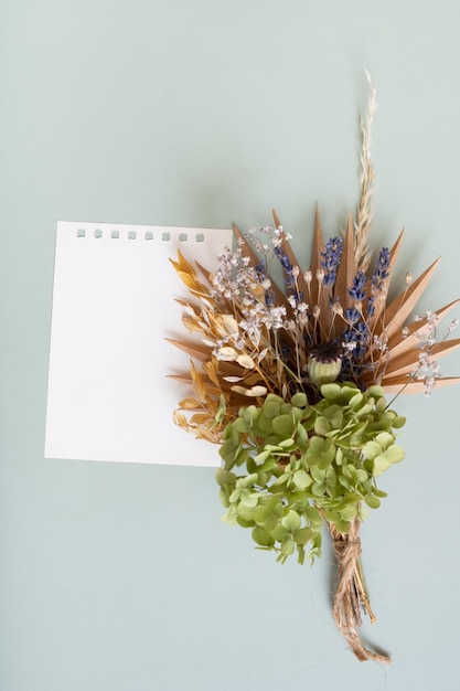 Papel em branco para notas e um buquê de flores secas e ervas em um fundo colorido