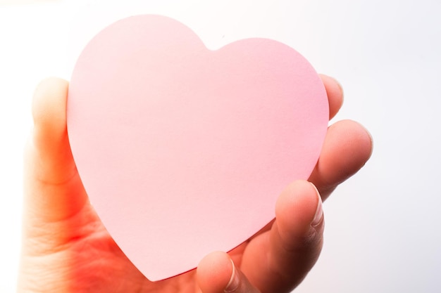Papel en forma de corazón de color rosa en la mano sobre fondo blanco.