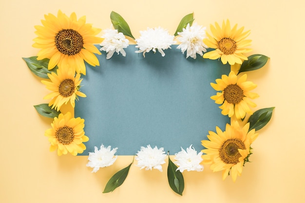 Papel gris en blanco rodeado de flores sobre un fondo amarillo