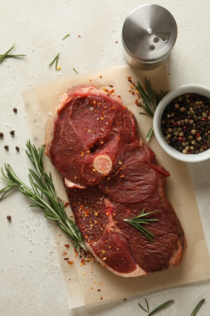 Foto papel para hornear con carne cruda, hierbas y especias sobre textura blanca